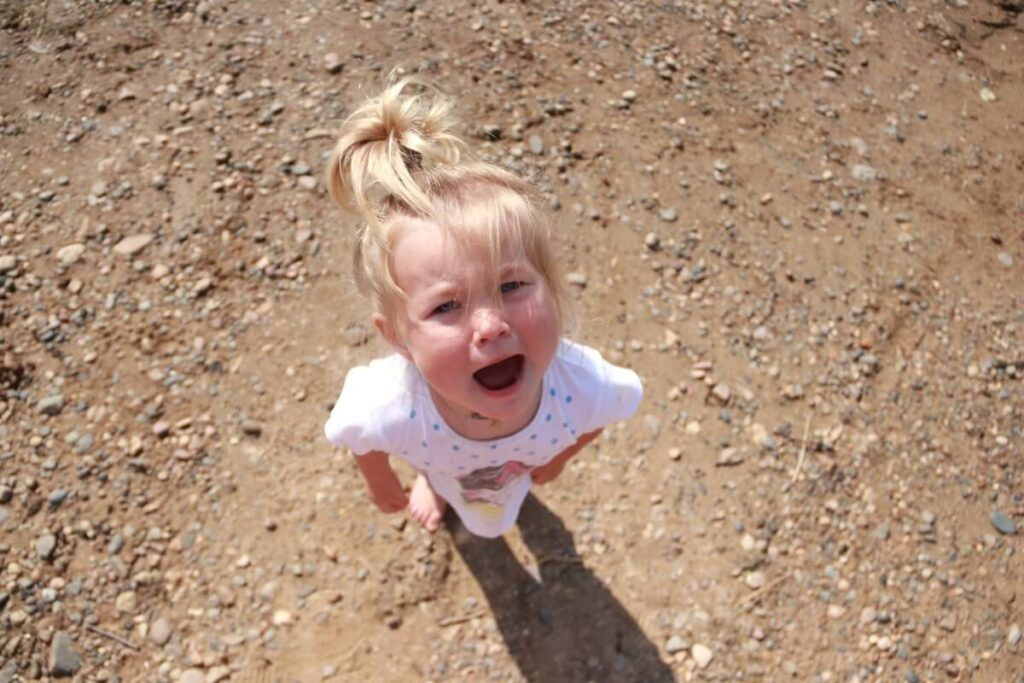 Mała dziewczynka patrzy w górę z otwartymi ustami na tle ziemi, wyglądająca jakby cierpiała z powodu syndromu DDA, choć być może po prostu się bawi.