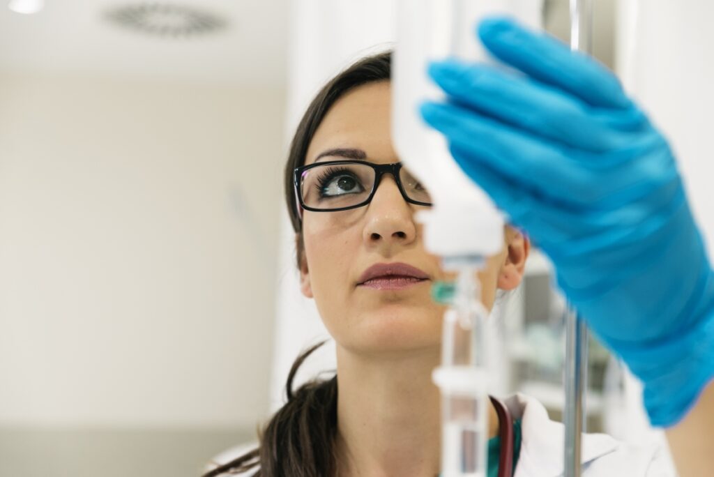 Kobieta w rękawiczkach sprawdza kroplówkę dla pacjenta z alergiami.